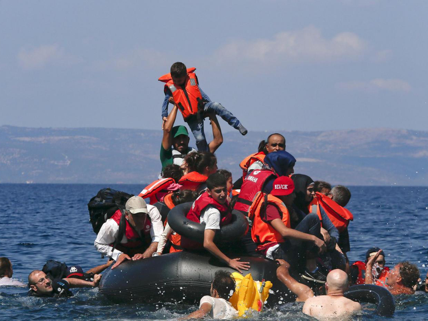 A refugee raises a child into the air as Syrian and Afghan refugees are seen on and around a dinghy that deflated some 100m away before reaching the Greek island of Lesbos, September 13, 2015. Of the record total of 432,761 refugees and migrants making the perilous journey across the Mediterranean to Europe so far this year, an estimated 309,000 people had arrived by sea in Greece, the International Organization for Migration (IMO) said on Friday. About half of those crossing the Mediterranean are Syrians fleeing civil war, according to the United Nations refugee agency. REUTERS/Alkis Konstantinidis